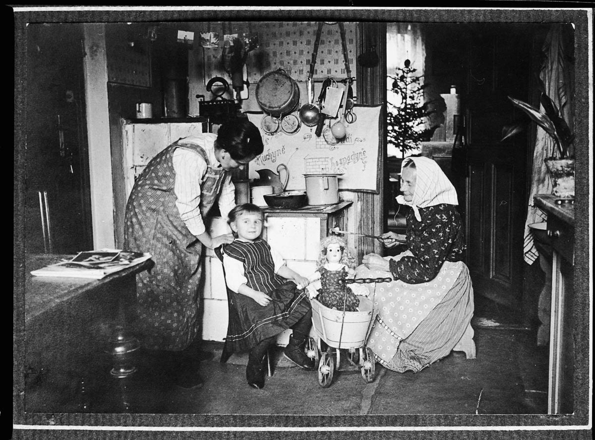 Two women and a girl by a coal stove in a Prague kitchen. The girl sits beside a doll in a pram. (Photo by Jan Honzak/Scheufler Collection/Corbis/VCG via Getty Images)