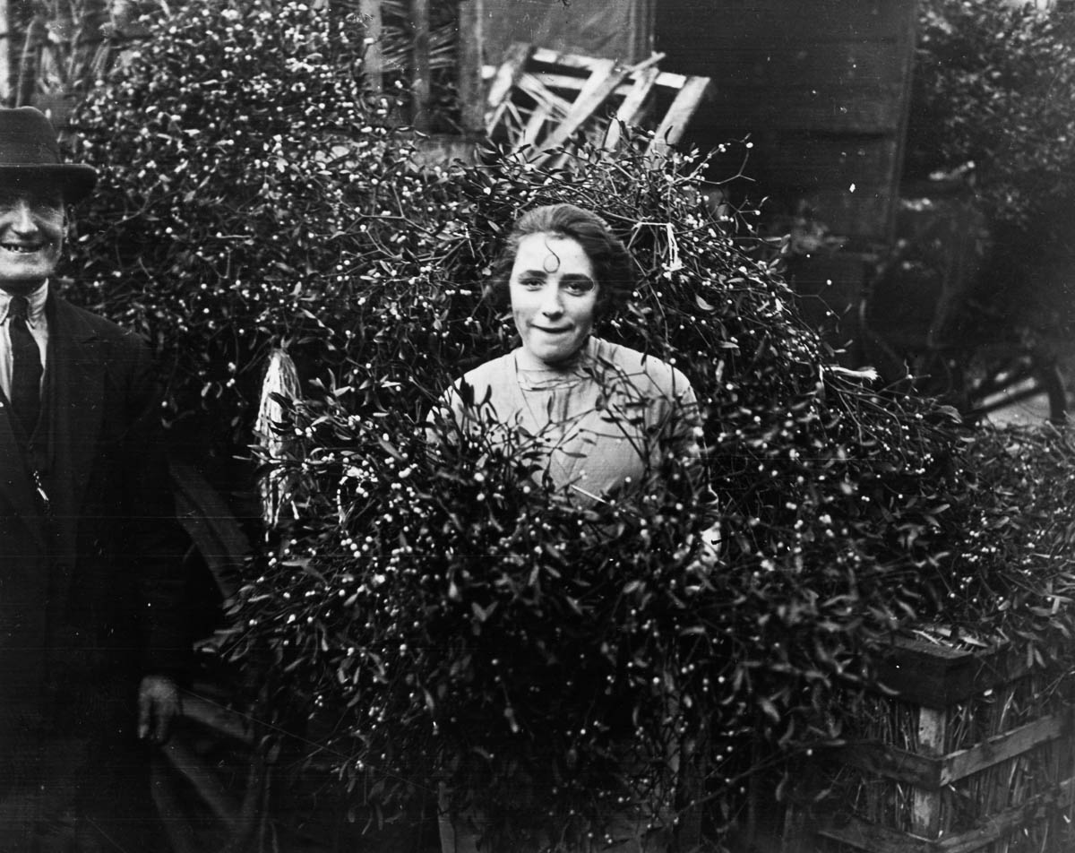 17th December 1928: A couple standing amongst the first delivery of mistletoe at Covent Garden market, London. (Photo by H. F. Davis/Topical Press Agency/Getty Images)