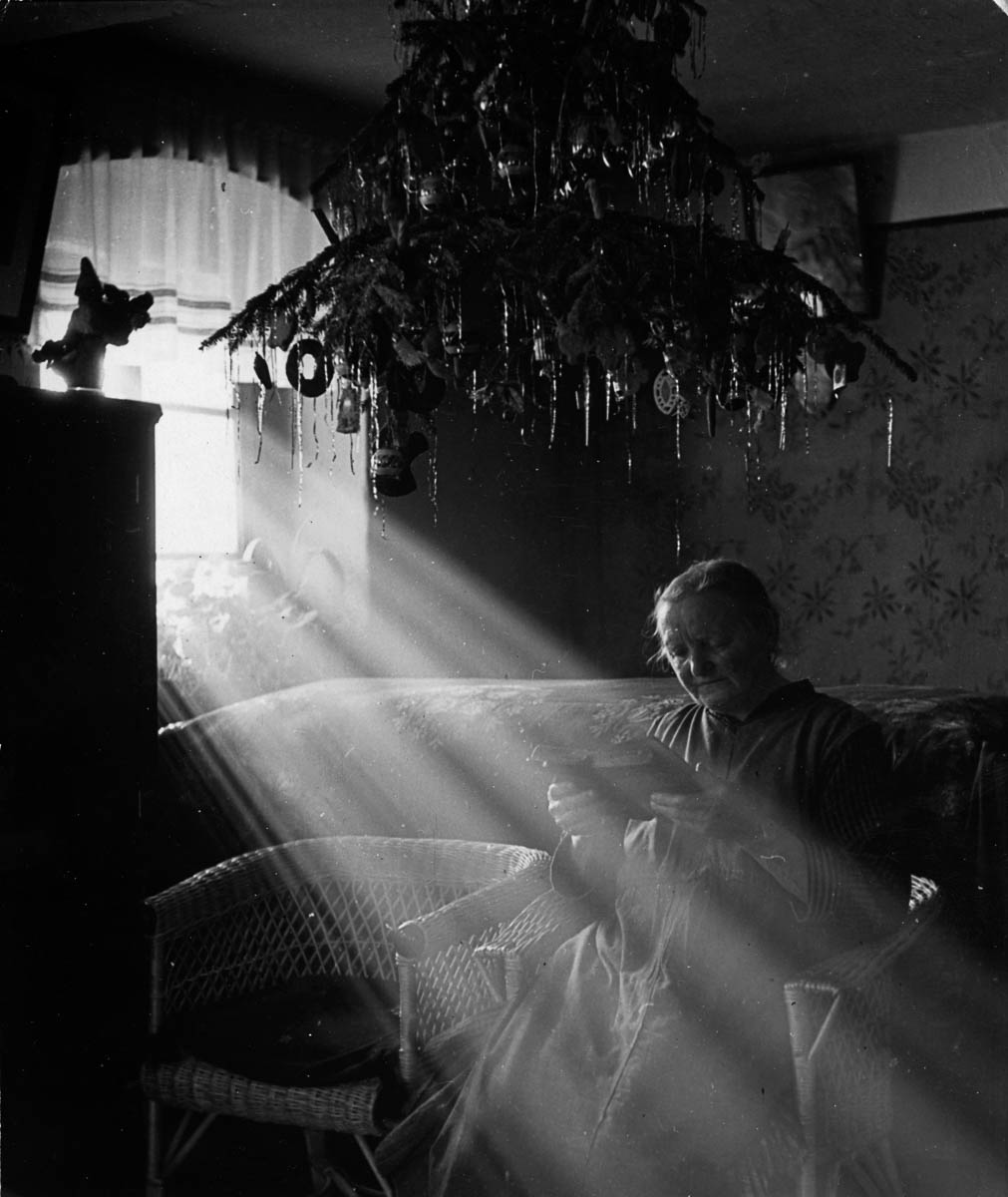 circa 1938: An old Czech woman sits in a shaft of light from a window, overhead hangs a decorated Christmas tree. (Photo by Hulton Archive/Getty Images)
